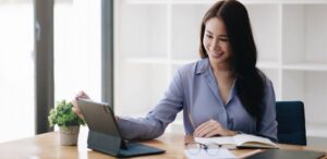A young professional woman smiles as she works on her laptop and notebook